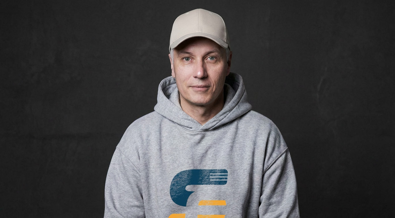 Stefan Frech sitzt in Casual Klamotten vor einem dunklen Hintergrund